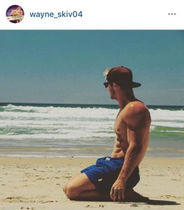 Super Dad Wayne Skivington kneels on beach in shorts