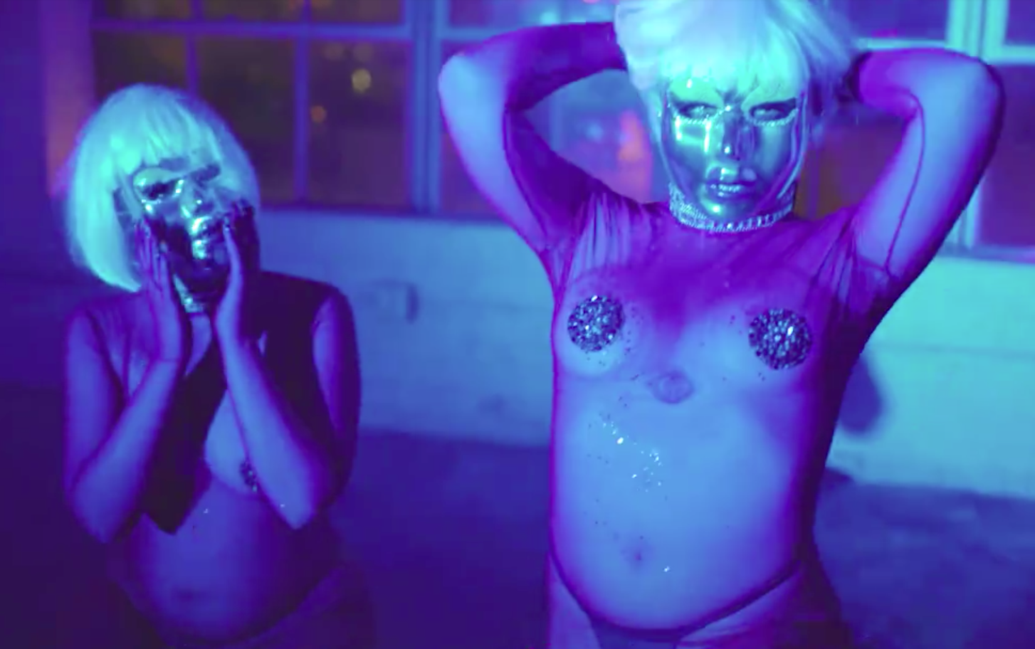 Two women in lady drag lit with blue light in blonde wigs wearing sheer outfits
