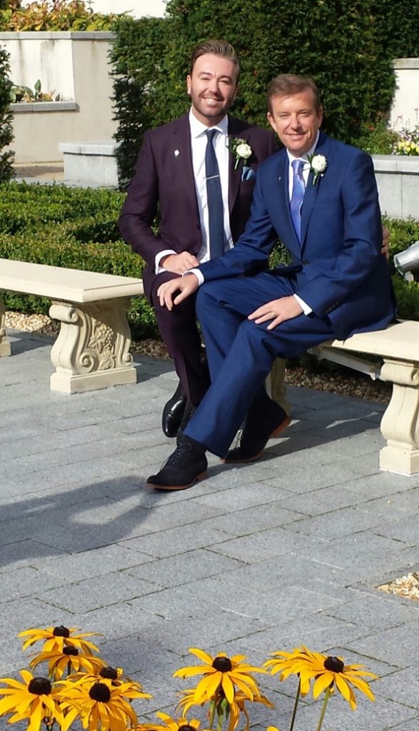 Alan Hughes and Karl Broderick got married and here the couple are in suits in front of a tree.