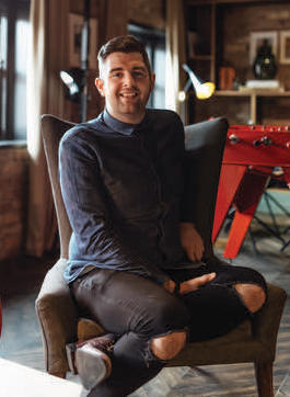 Marty Campbell sitting in an armchair with jeans with rips in them for the dean hotel and sophie's amuse bouche