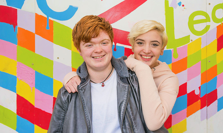 Cody and Aiden standing in front of a colourful background, who are two young irish lgbt people