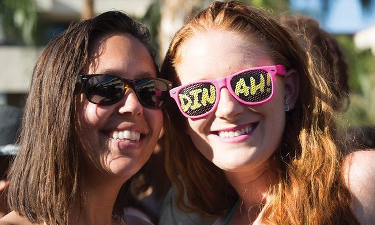 2 girls at the Dinah Shore Weekend with sunglasses and the word dinah written on one pair of glasses, Dinah being one of the top ten queer travel events of 2017