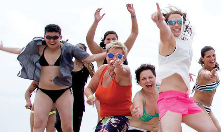 Woman in beachwear jumping and smiling at Ella International Lesbian festival, one of the top ten queer travel events of 2017