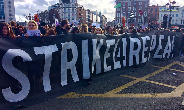 People holding a sign saying strike for repeal to repeal the 8th amendment which is an issue which would likely be impacted by a diaspora postal vote