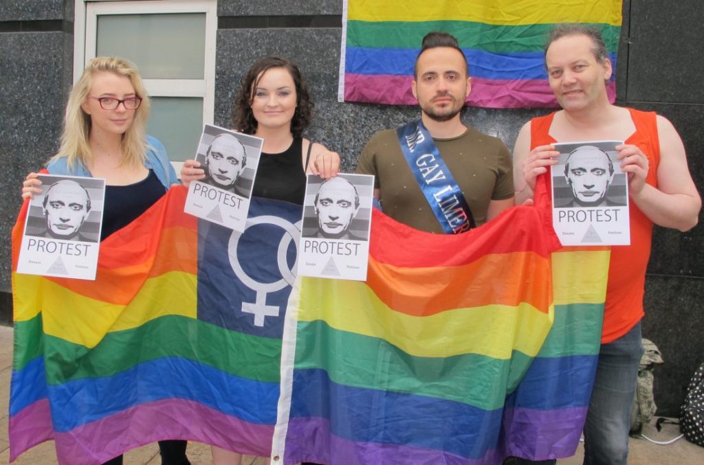 Dr Christian Moretti who is the current Mr Gay Limerick holding a big rainbow flag with other people who will be at Mr & Ms Gay Limerick event by Limerick Pride