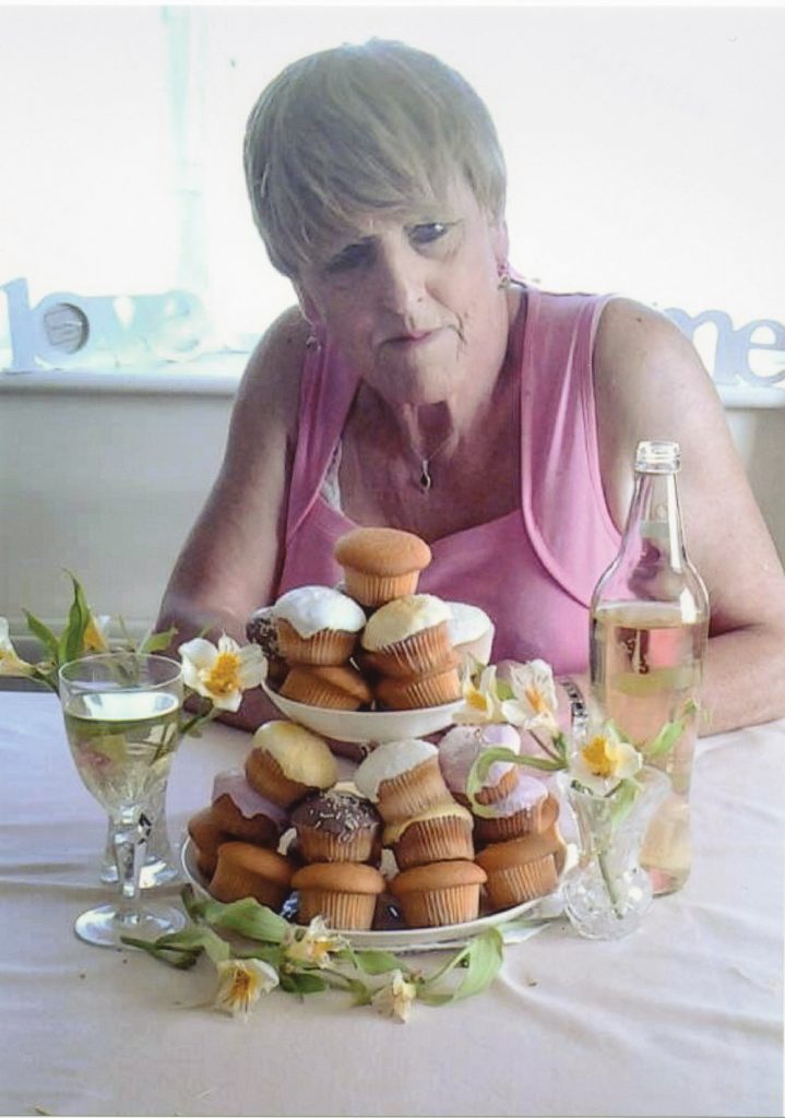 Christine Beynon from the art exhibition in Becoming Christine sitting in front of a stack of cupcakes