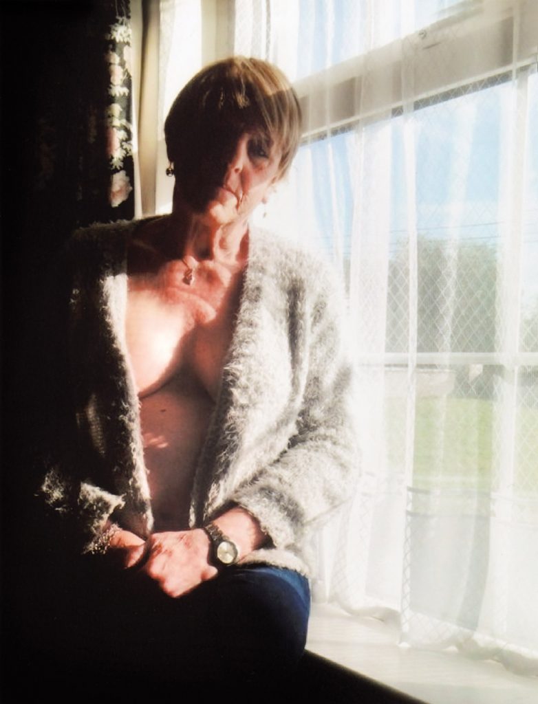 Christine Beynon from the art exhibition in Becoming Christine sitting by a window with net curtains