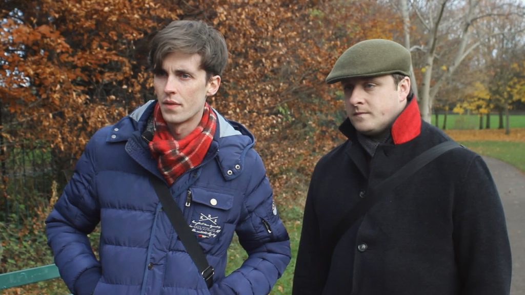 Maurice and Kenny from Awful Gays standing in a park with trees in the background in coats
