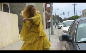 Trans Beyoncé Impersonator smashing a car window with a baseball bat from the outside
