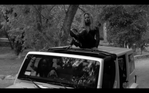 Trans Beyoncé Impersonator on top of a car in black and white with thigh-high boots