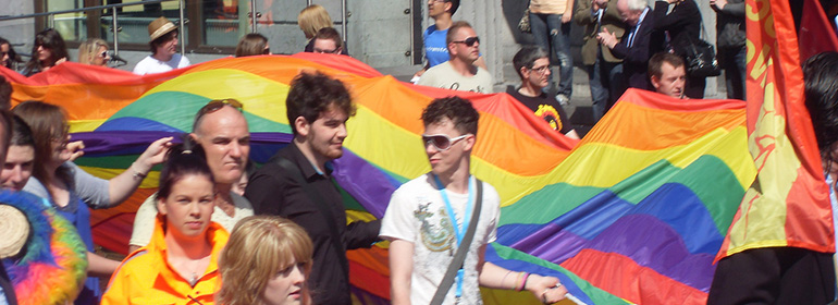 The GCN Galway pride 2016 guide has information on when the Galway Pride Parade 2016 is on, which is pictured here with men and women and a giant rainbow flag