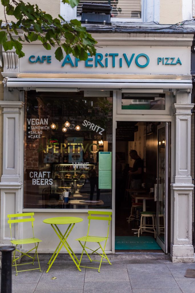 A portrait photo of Aperitivo on Parliament street from the outside, with green table and chairs on the street