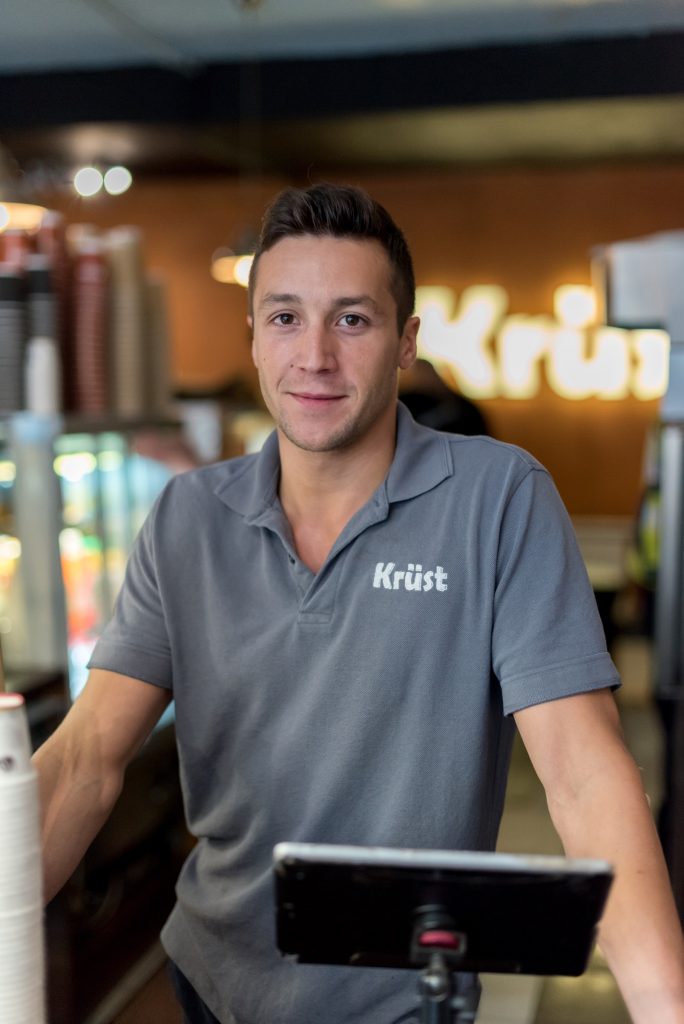 Krüst Bakery's manager standing in front of the glowing Krüst Bakery logo