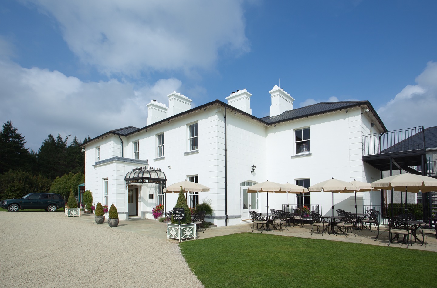 An exterior shot of the lodge at ashford castle where if you book a wedding, you could win a luxury cruise to the value of e10000 with white walls, parasols, green grass and blue skies