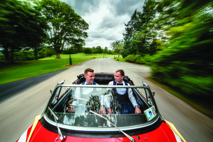 Andrew and thomas driving in a red convertible from Andrew and Thomas' Real Weddings article