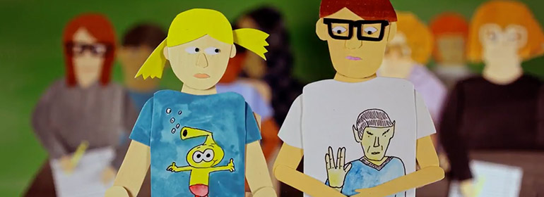 A scene from Torrey Pines the movie with a blonde person and guy in glasses sitting at a desk with characters on their t-shirts