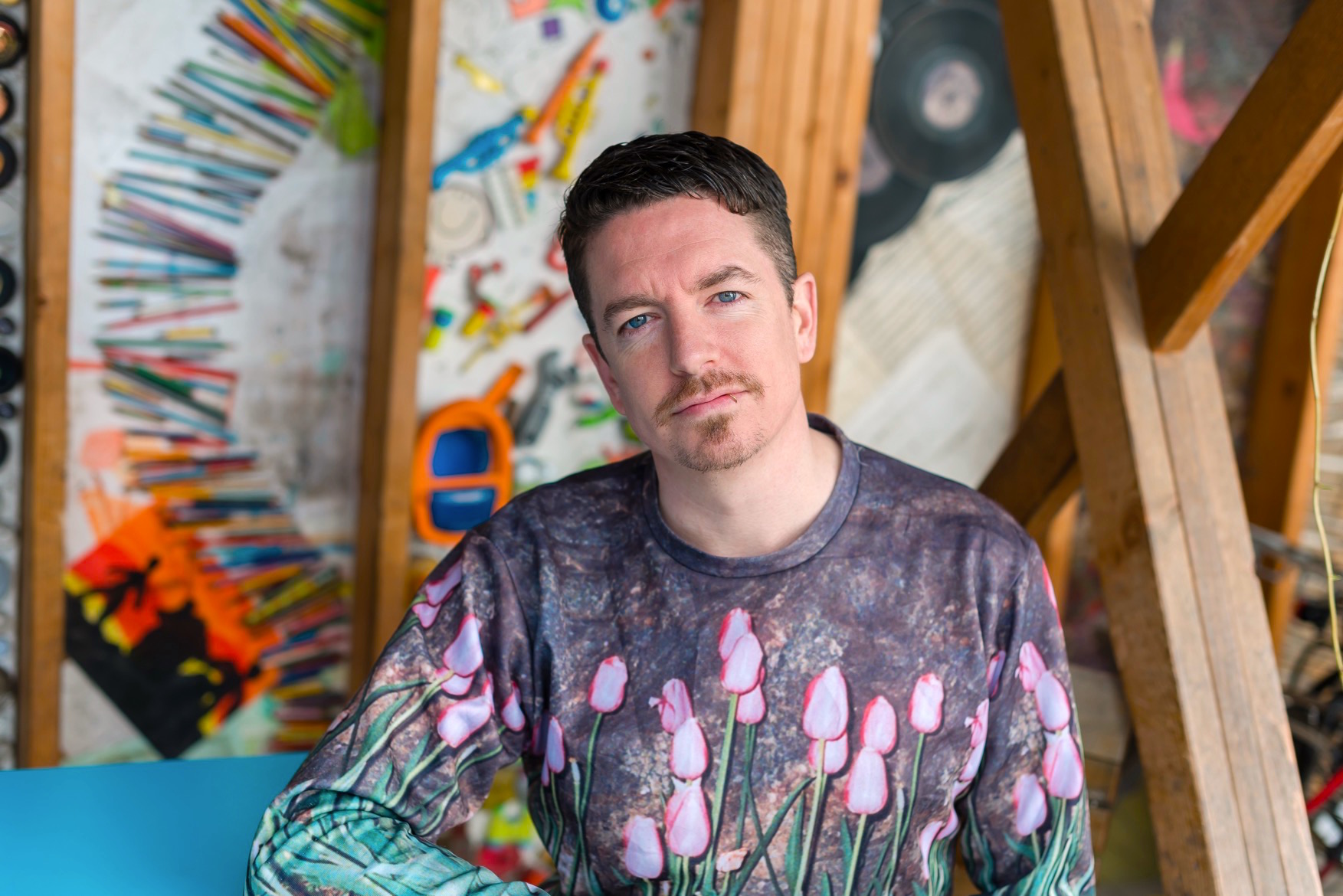 Ray O'Neill sitting outdoors in from too a painted wall at the cake cafe and slice which are both owned by Ray O'Neill