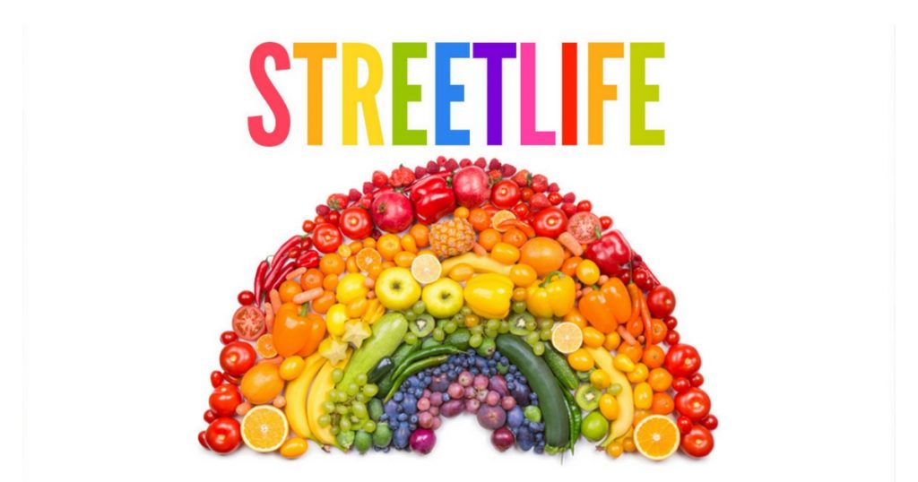 An array of vegetables in the shape and colour of a rainbow with the caption 'Street Life' written above it