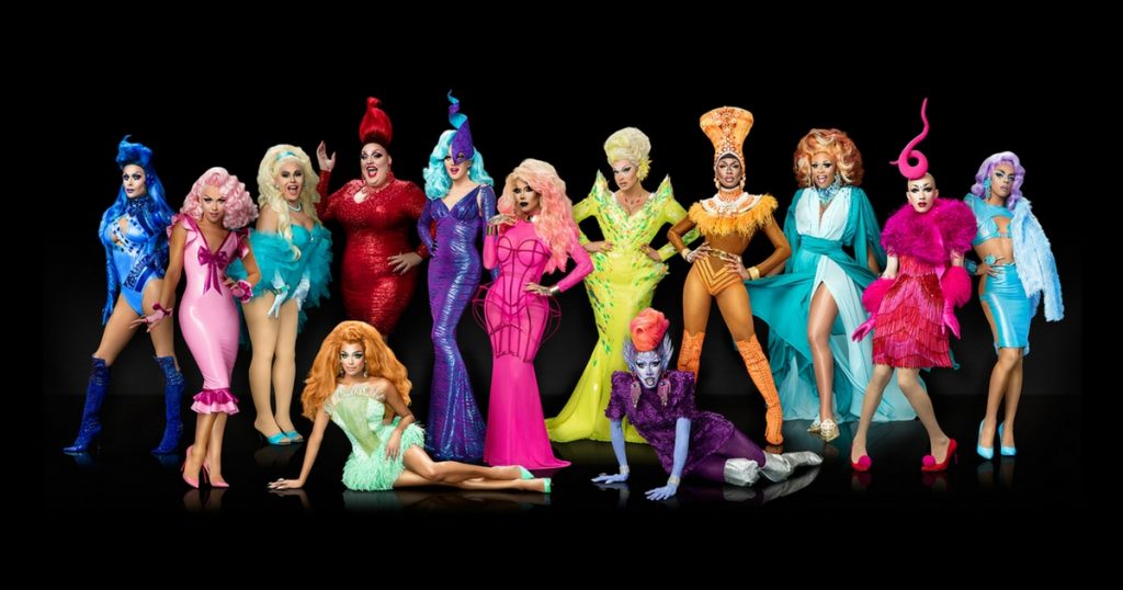 The Drag Queens competing in season 9 of Rupaul's Drag Race pose together in colourful outfits in front of a black back-drop.