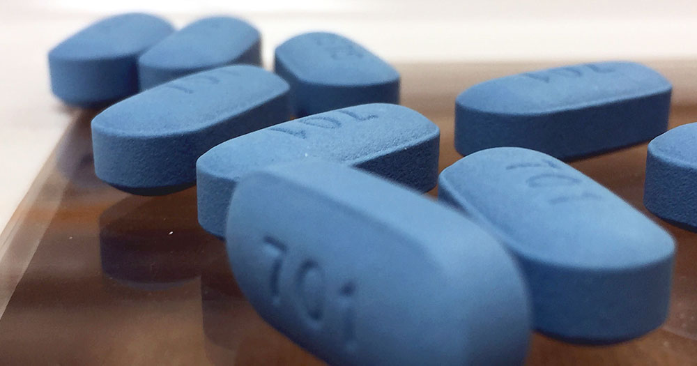 Several blue pills of the Gilead medication called Truvada laid out on a glass surface with the number 701 written on the front of them