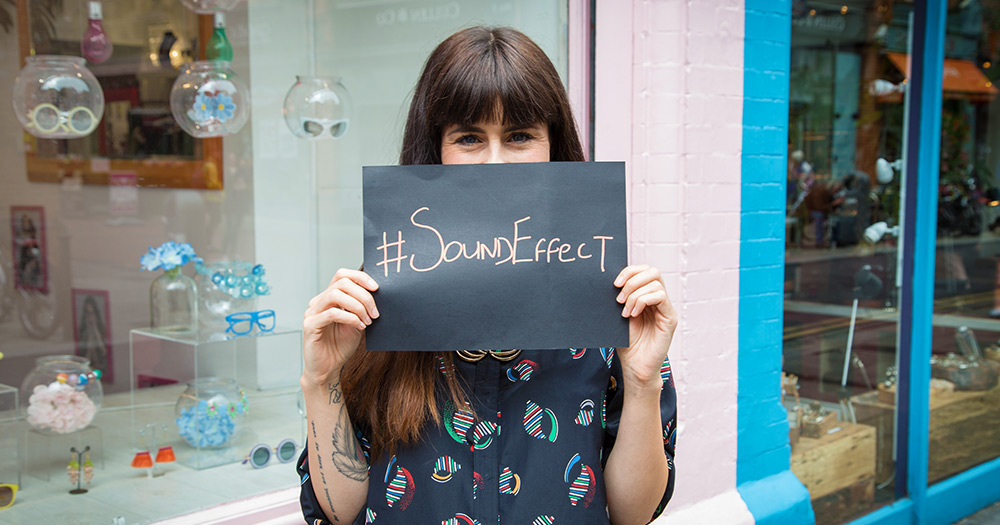 A woman holding a sheet of black paper that says #soundeffect
