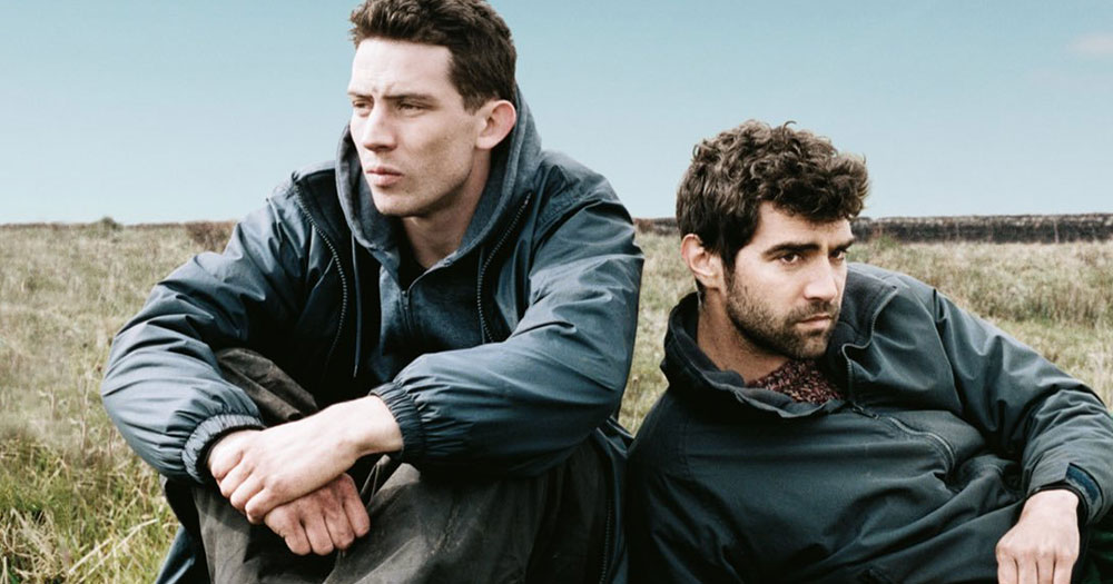 The two characters from God's Own Country sitting in jackets on country grass