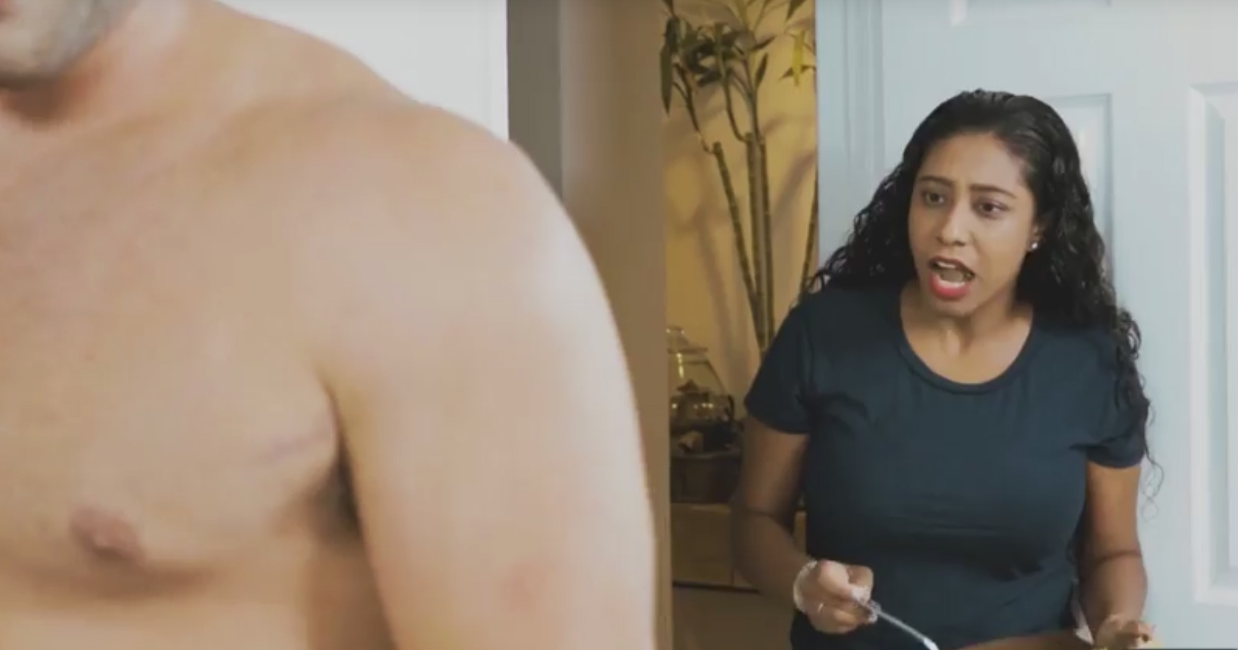 Close-up of a shirtless guy while Nikki V. looking shocked in the background