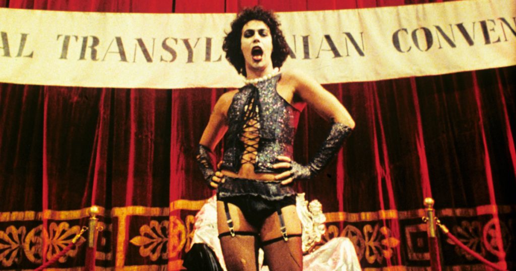 Dr Frank-N-Furter standing in front of a banner while singing. He is the top pick as most Iconic LGBT+ character in horror movies