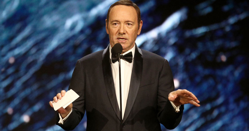 Kevin Spacey standing in a tux with cards in one hand