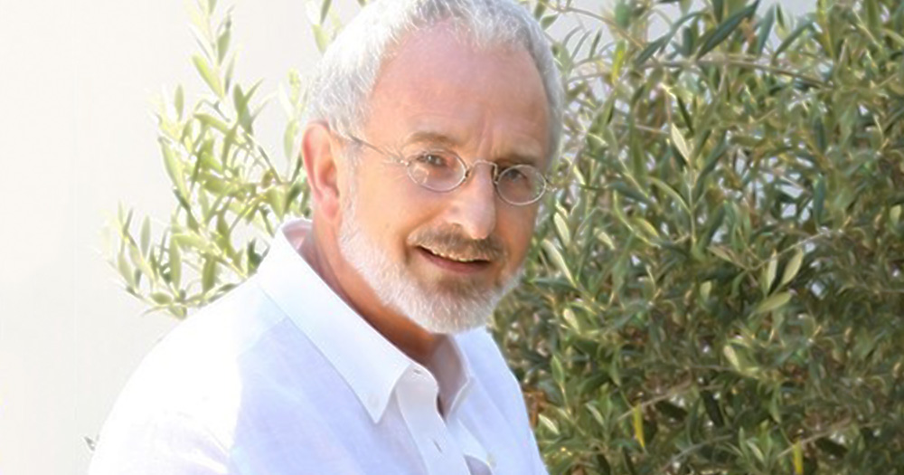 Michael Murphy smiling in a white shirt wearing glasses in front of a green plant
