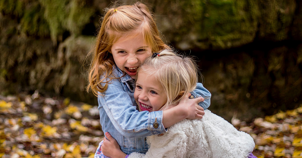 Children playing in a park with leaves on the ground behind them smiling because same-sex couples can now adopt even if they are not married.