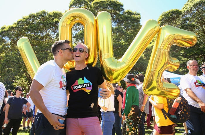 Two men kiss in front of balloons that spell out "LOVE"
