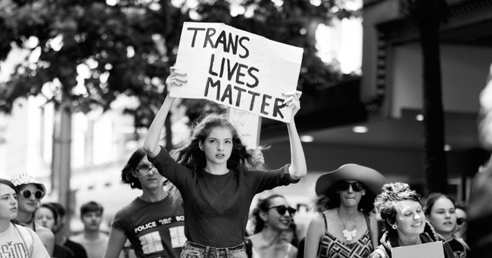 callout for newstalk: a girl holding a sign that says "Trans Lives Matter".