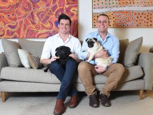 Photo of Ryan Bolger and Tim Wilson in their home with their two pet pugs