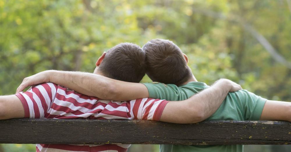 Two guys on sitting a bench hugging each other