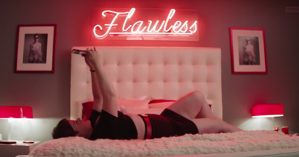 Heathers star lies on a bed a neon sign which reads flawless