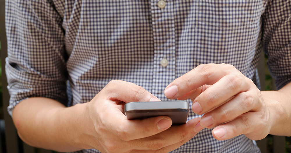 cork man charged: the chest of a man in a flannel shirt. He is holding a smart phone in his hands