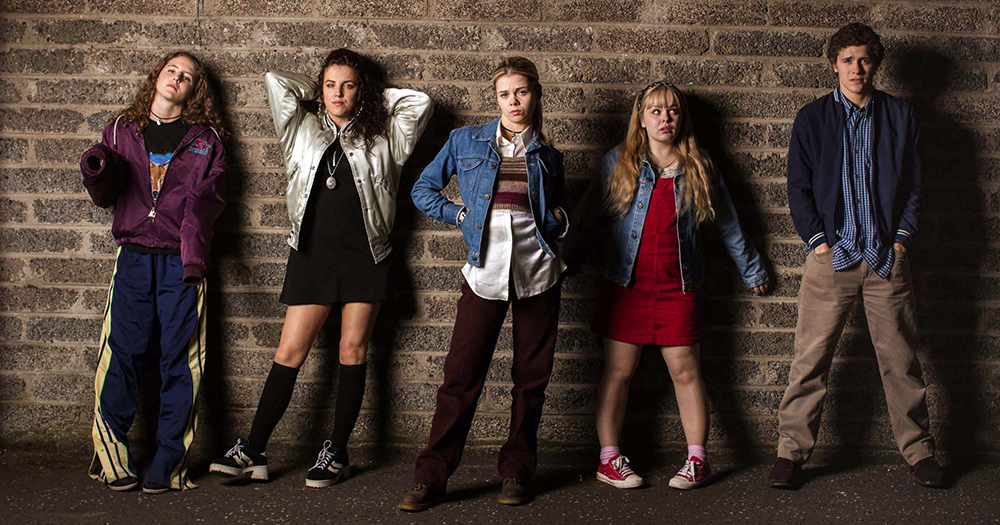 The cast of Derry Girls posing - behind them a brick wall
