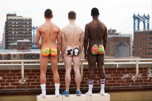 Three naked men with butts painted as Easter eggs standing on the roof of a building in New York