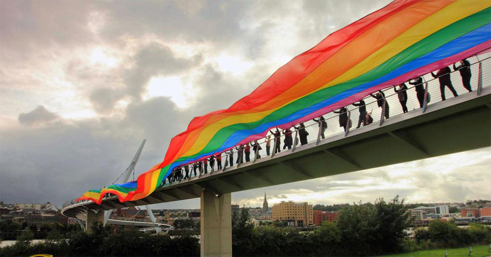 A group of people lined across the Foyle bridge holding a huge rainbow banner