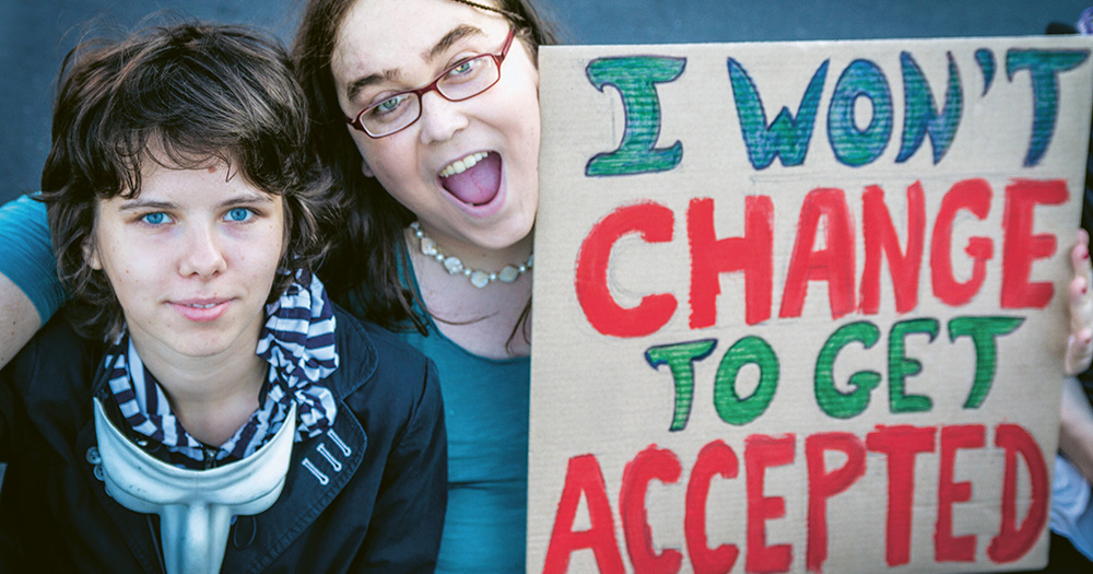Two transgender people hold a sign that says "I won't change to get accepted"