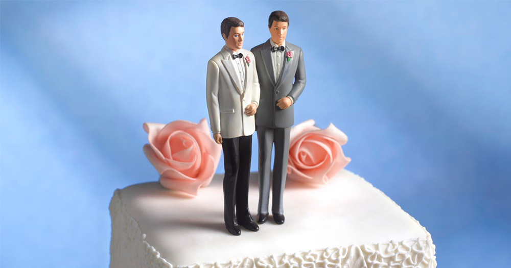 A wedding cake with figurines of a gay male couple on top
