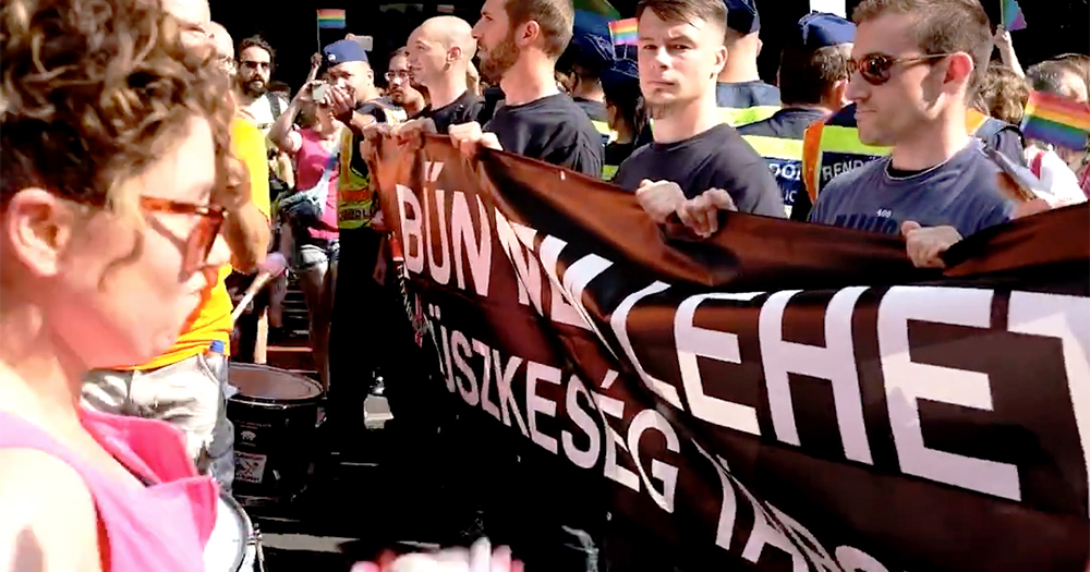 A group of male fascists holding a black banner blocking the progress of a Pride parade