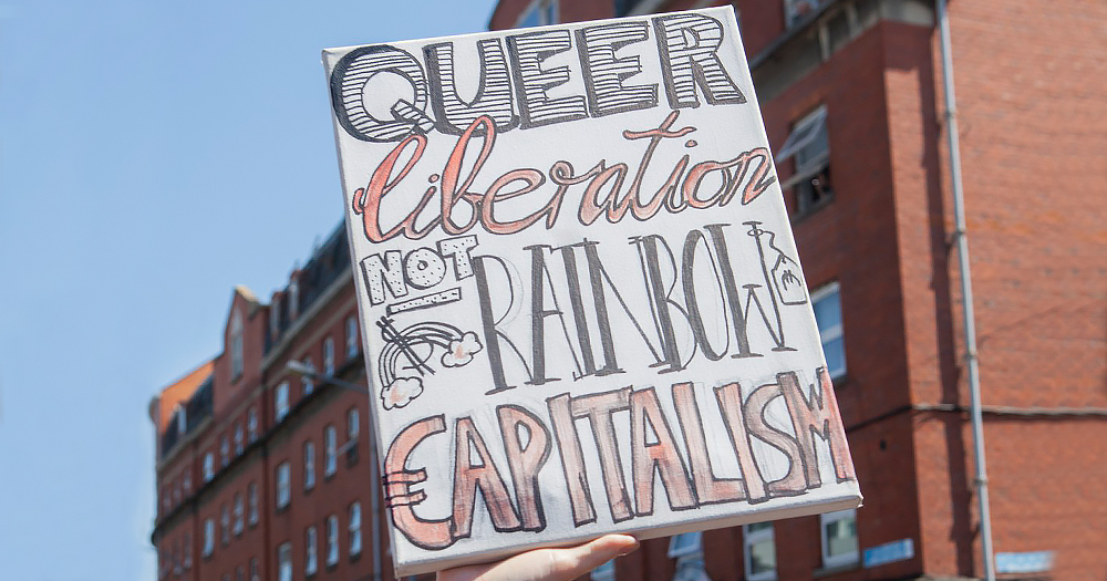 Petition launch: Someone holds a sign which says: "Queer libeteration not rainbow capitalism"