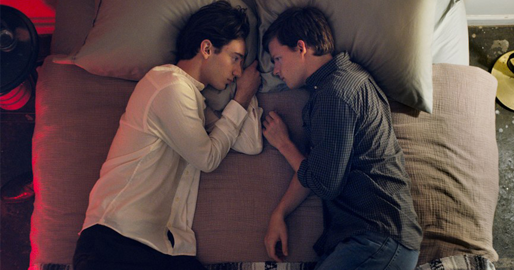A still from the film Boy Erased showing two fully dressed young men lying on top of a bed staring into each others eyes