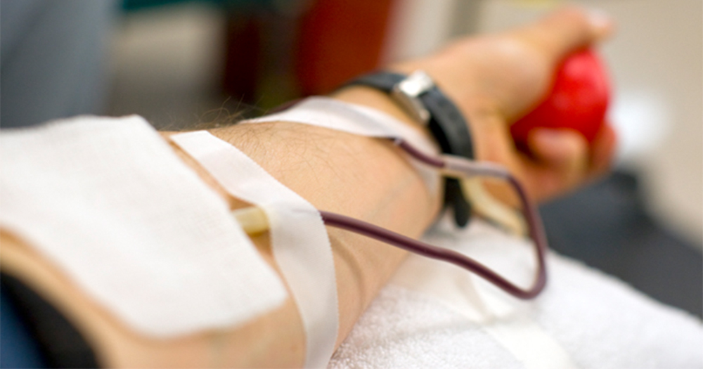 A close up image of a man's arm with IV tube filled with blood, his hand squeezing a ball