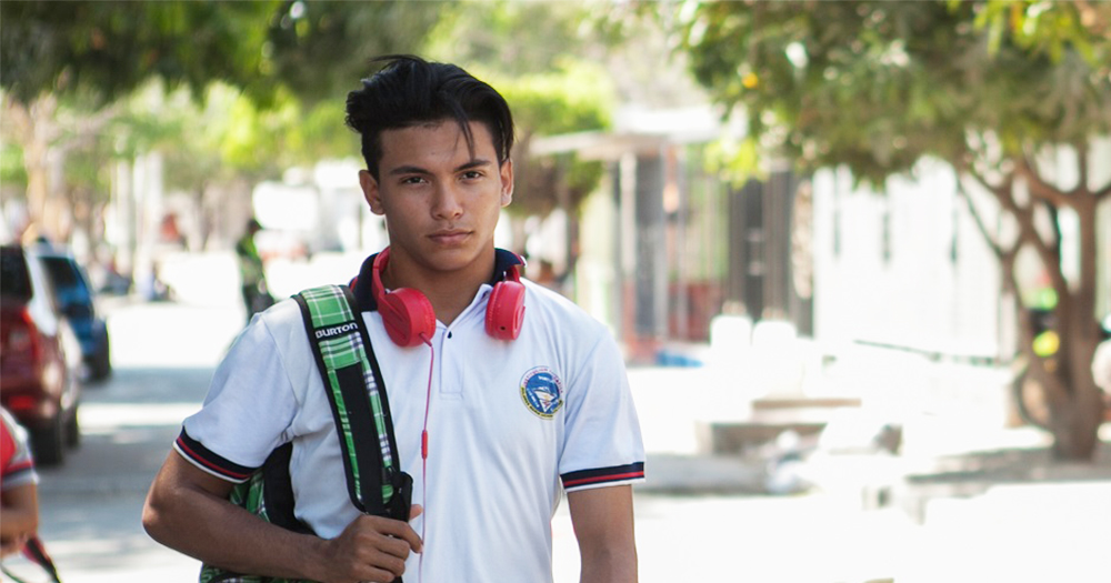 A still from the film 'Dario' competing for the Iris Prize showing a young man walking down a sunny street with a backpack slung over his shoulder