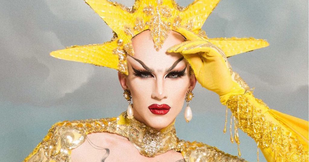 Sasha Velour wears a yellow crown and yellow gloves.