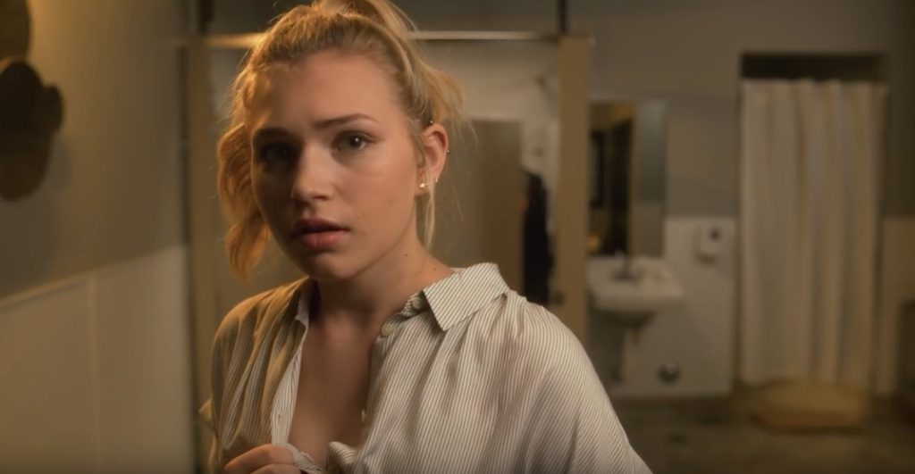 A still from the anti-trans video depicting a young woman changing clothes looking toward the viewer with a terrified expression as a cubicle door swings open behind her