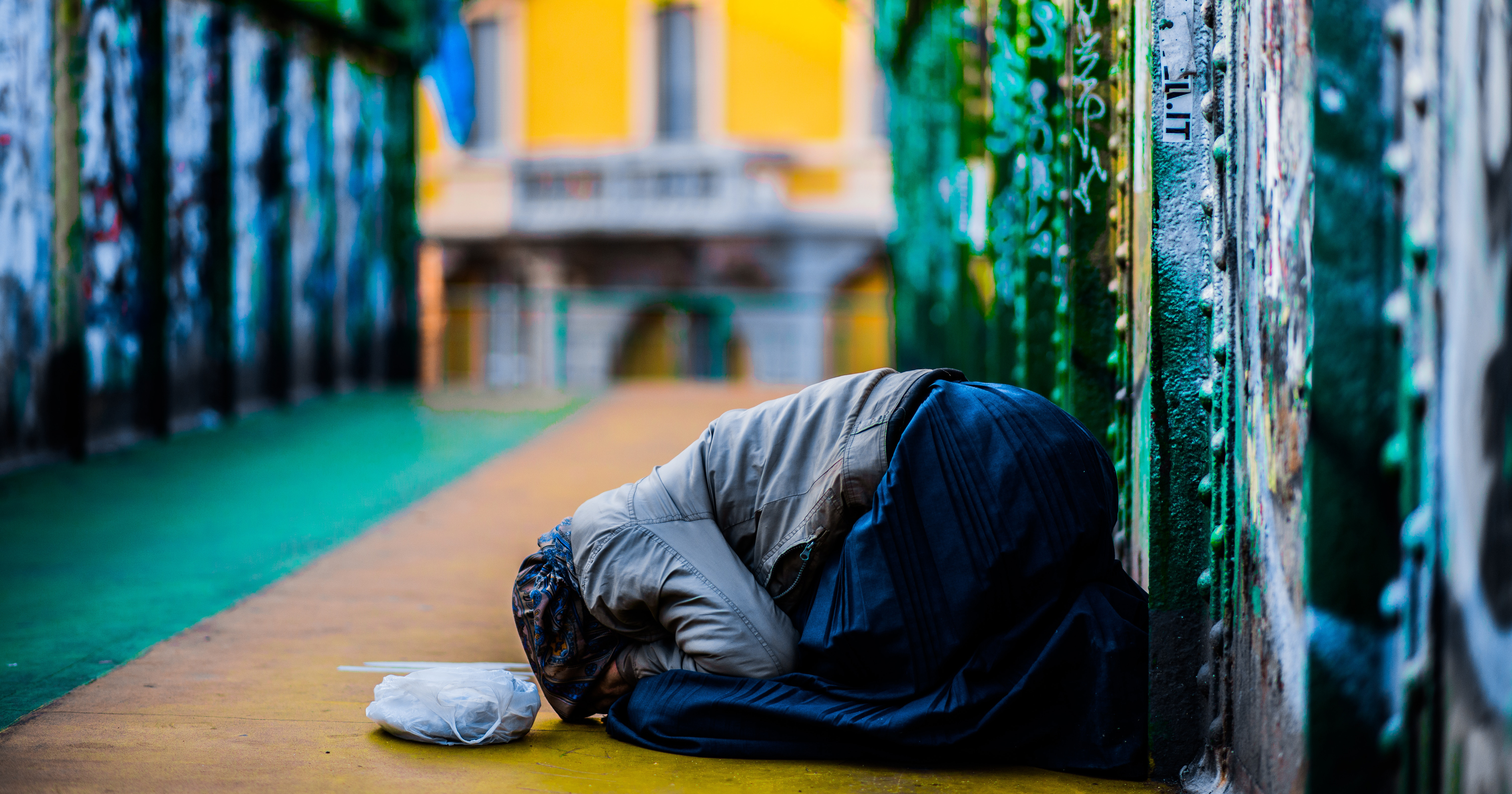 On a bridge, a kneeling homeless women leans over, hiding her face